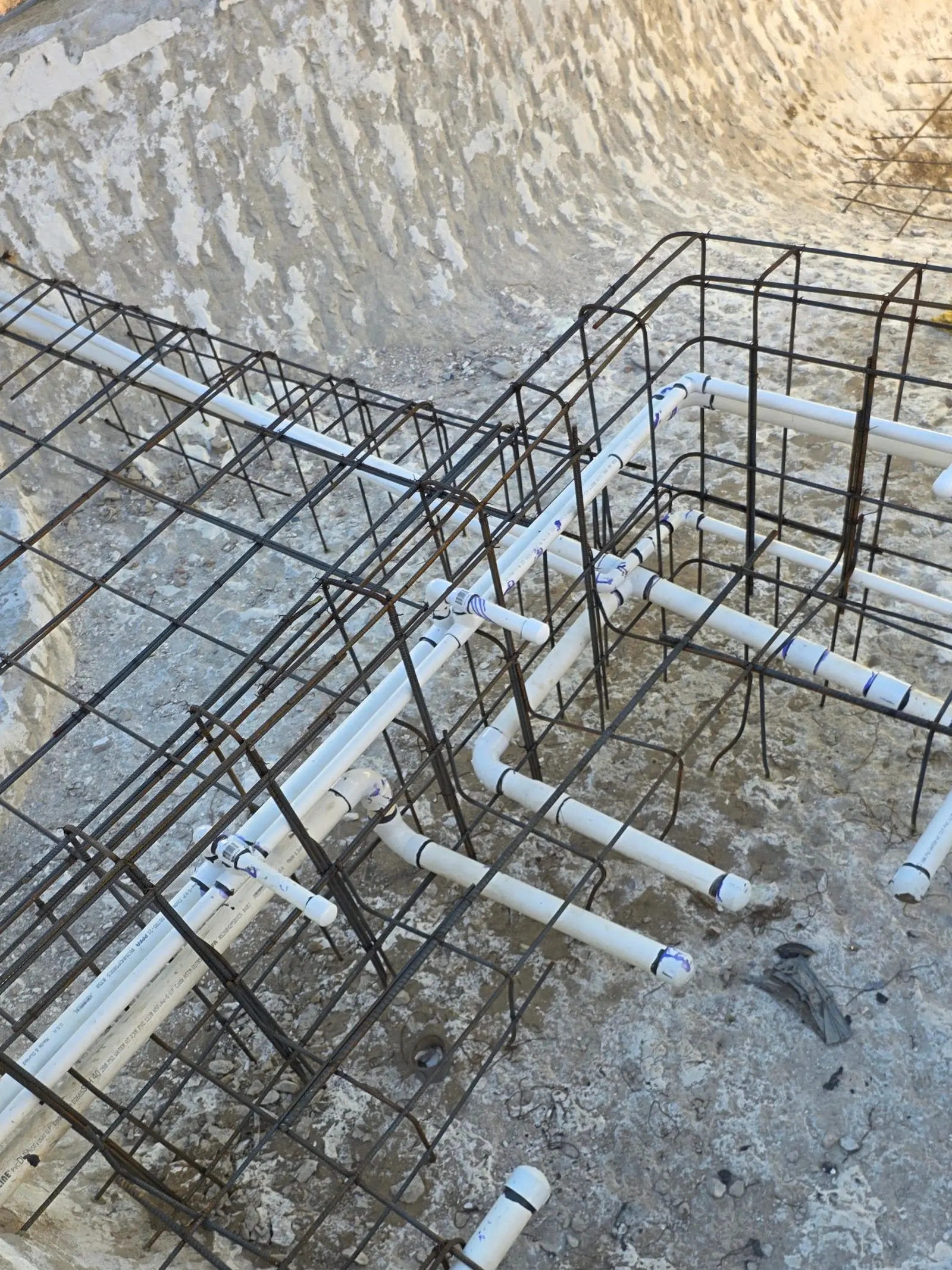 White PVC pipes with capped ends running through steel rebar cages in an excavation with a curved earth wall